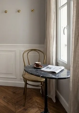 Coin repas — guéridon marbre, chaise Thonet, patères laiton alignées sur le soubassement.